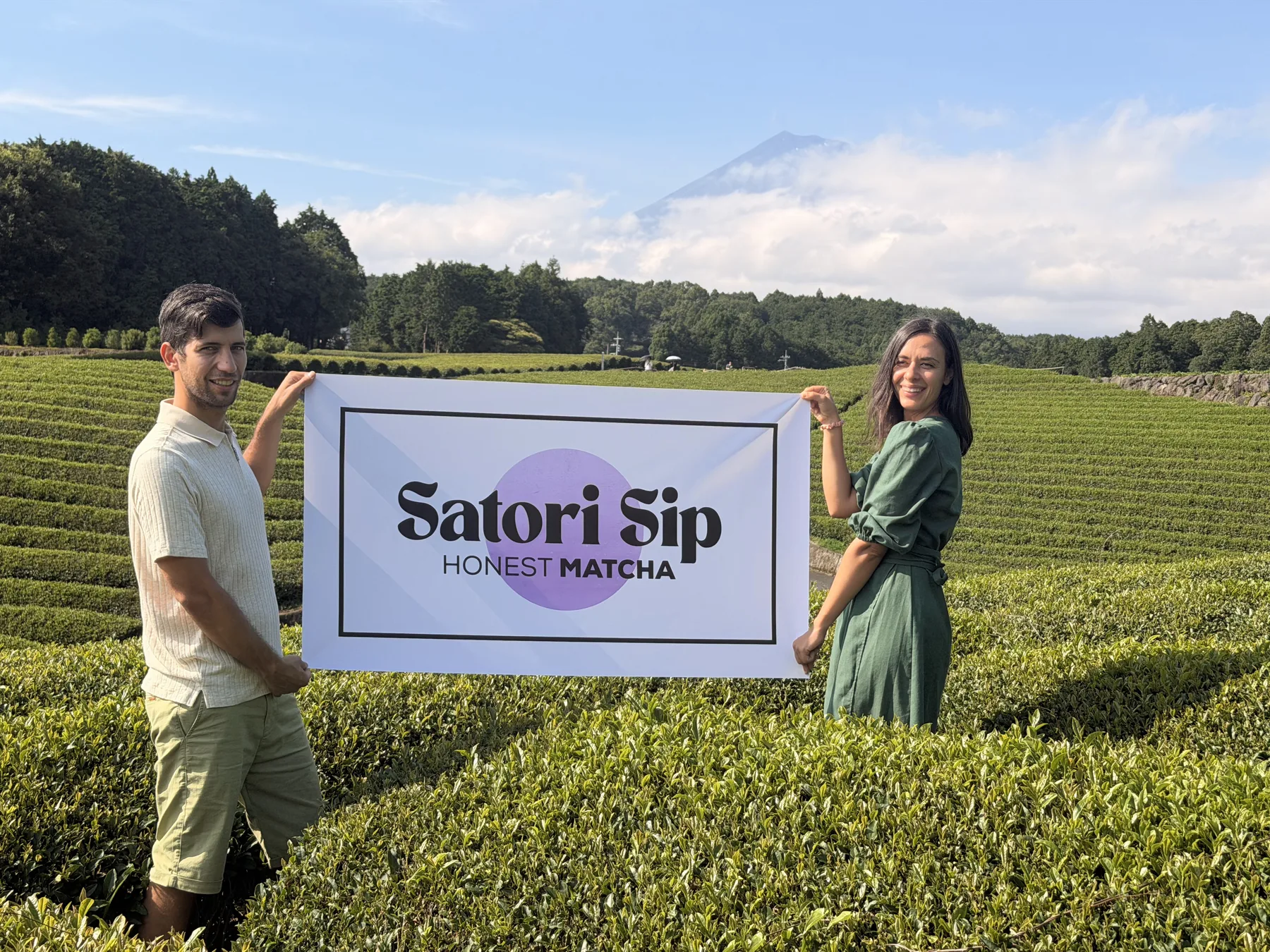 Viktor and a partner holding the Satori Sip banner in a Japanese tea field with Mount Fuji